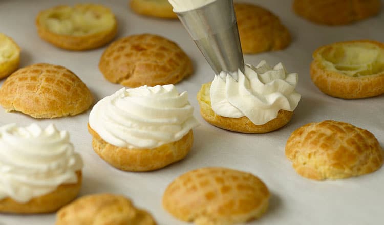 Piping diplomat cream onto cream puff bottoms.