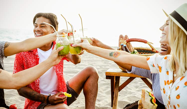 People "cheersing" on the beach with drinks and snacks