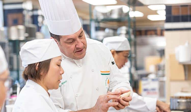 A chef helping a student in the kitchen.