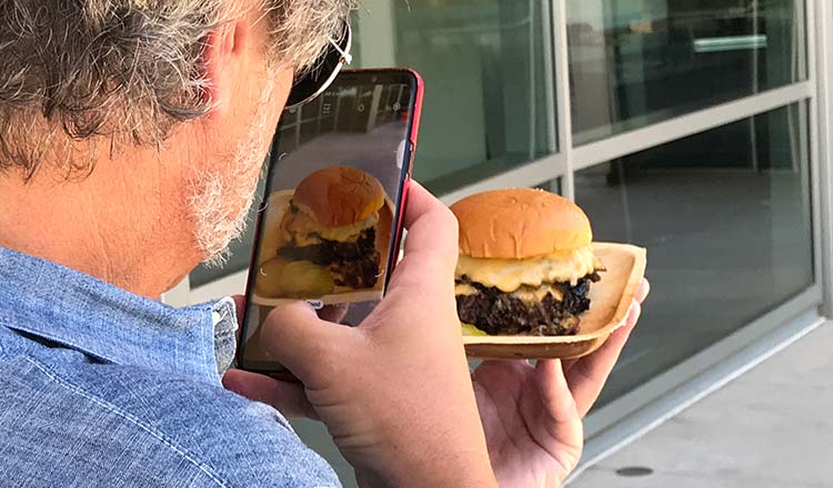 Man taking cellphone photo of a hamburger.