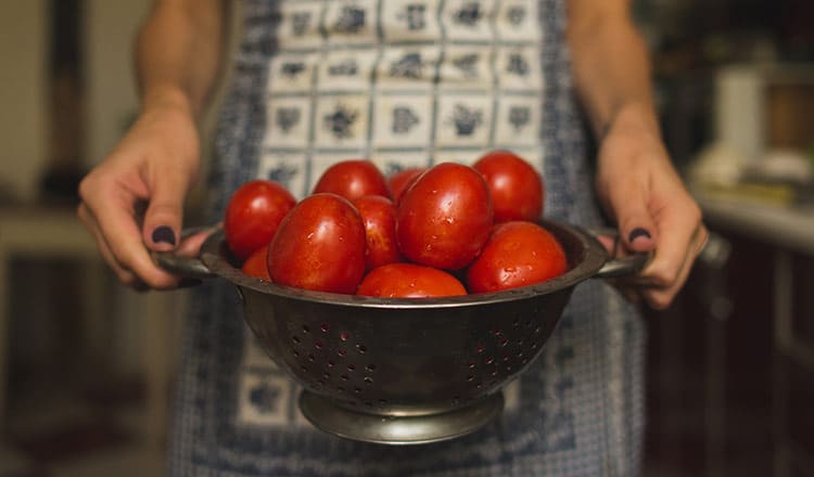 A person in an apron holding a strainer full of Roma tomatoes