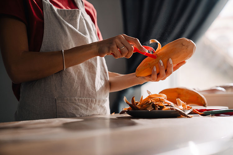 Woman in apron peeling sweet potatoes
