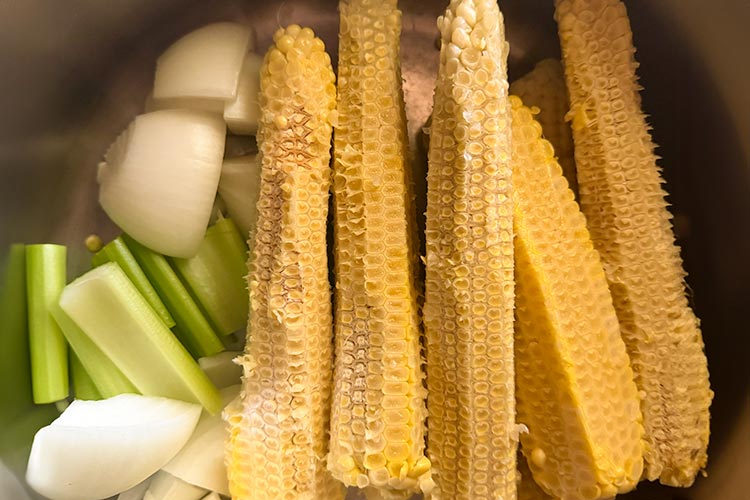 Corn cobs in a pot with sliced onion and celery.